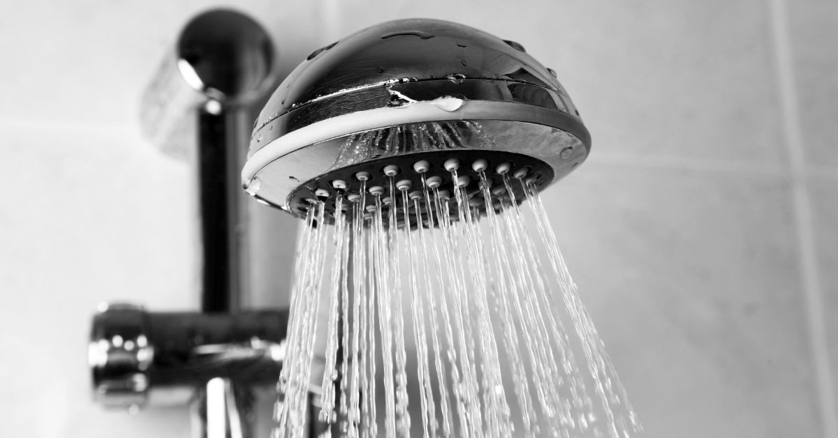 Close-up of a dripping shower head with steady water flow indicating a leaking shower problem.